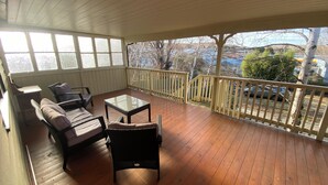 Un porche cubierto con suelo de madera, una mesa de vidrio, muebles de mimbre y vistas al exterior.