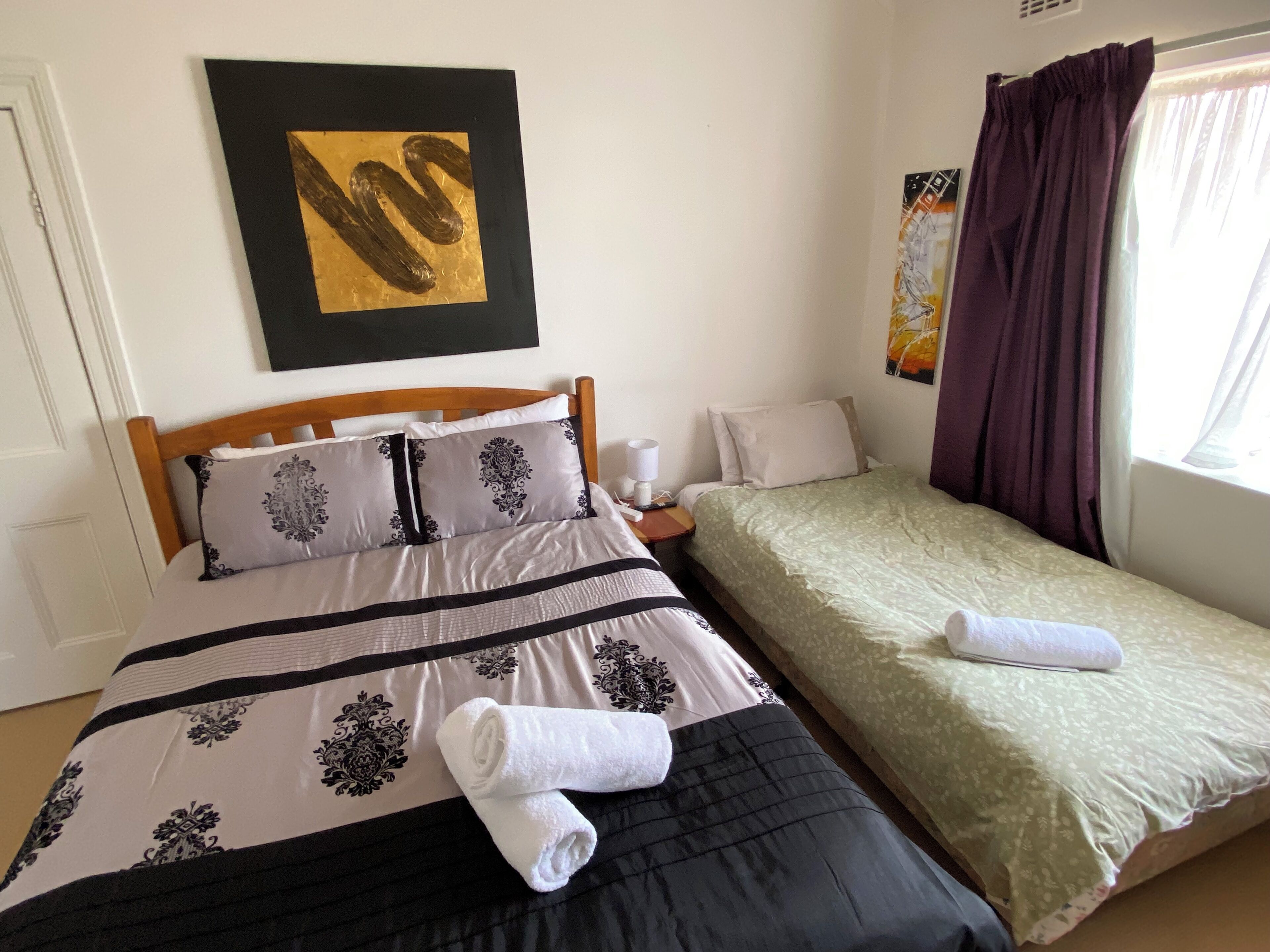 A bedroom with a large bed, a smaller bed, and a nightstand with a lamp.