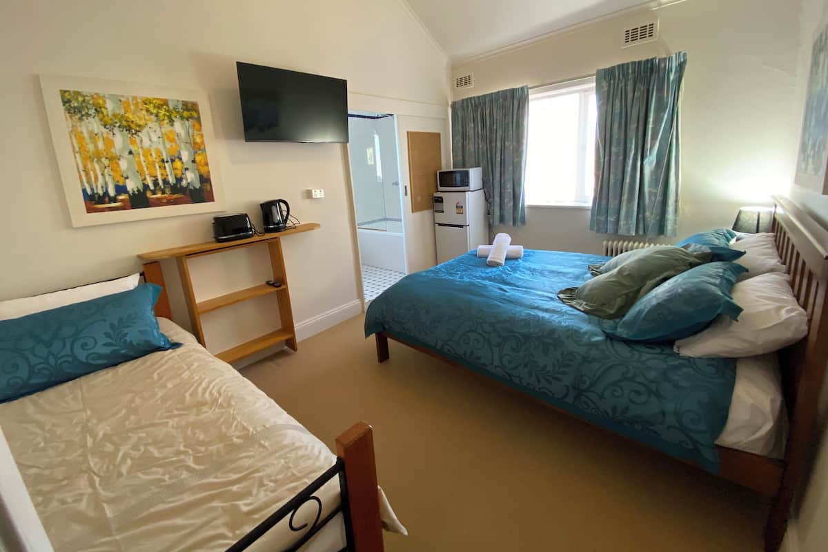 Habitación de hotel con dos camas, un escritorio, televisión, microondas y baño visible a través de una puerta de cristal.
