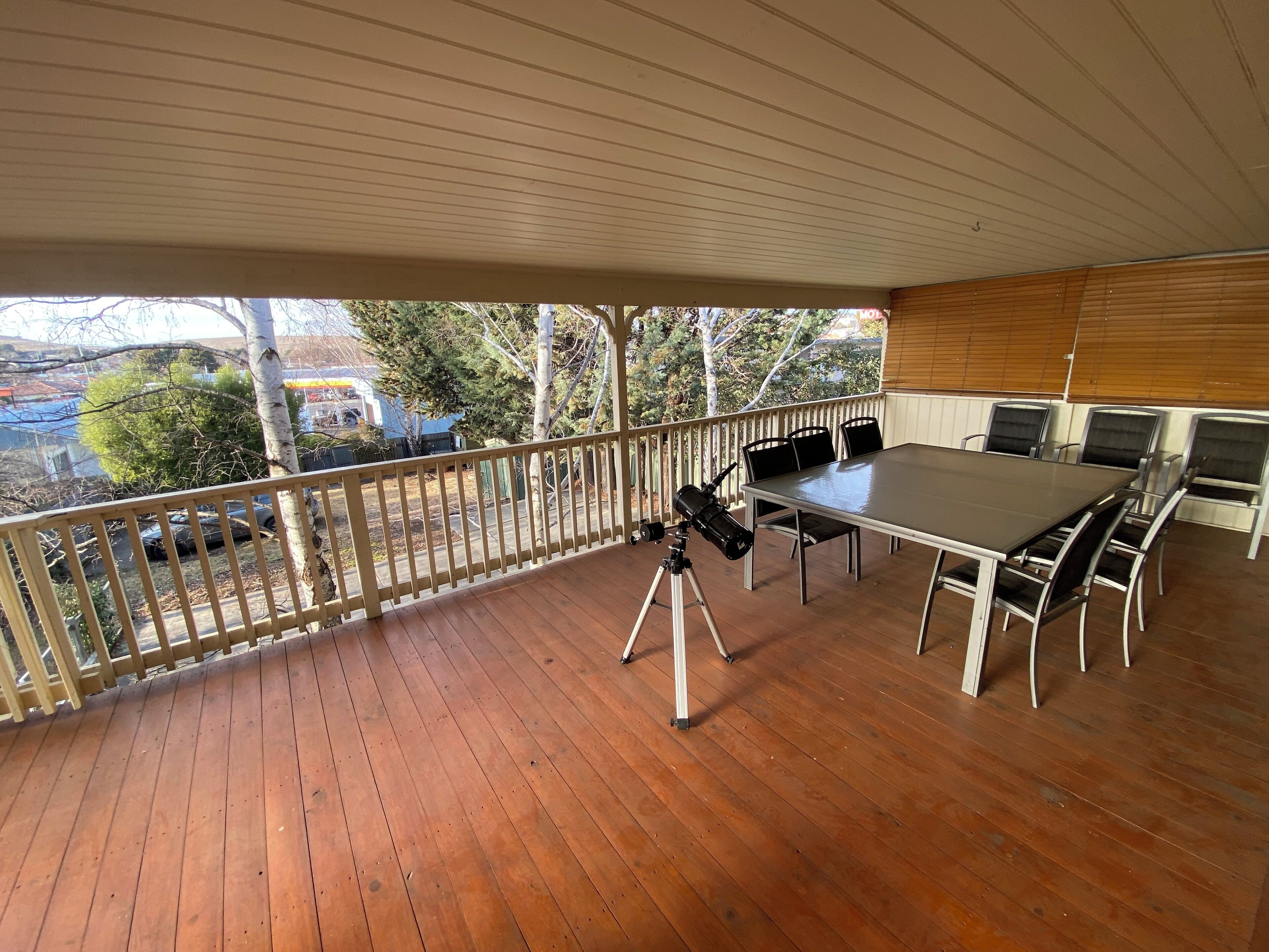 An outdoor deck with a wooden table and chairs, a telescope, and a view of a residential area.