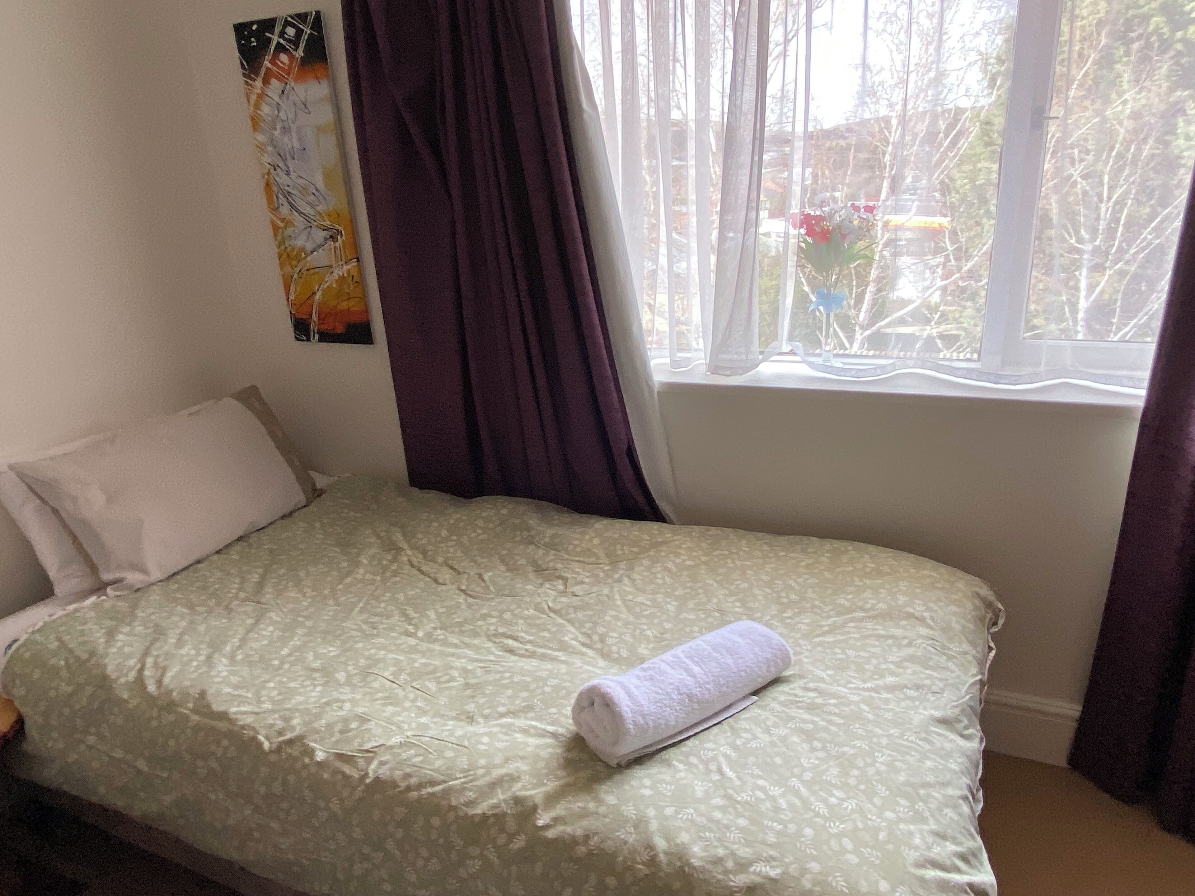 A bed with a floral bedspread, a rolled towel, a pillow, and a window with curtains.