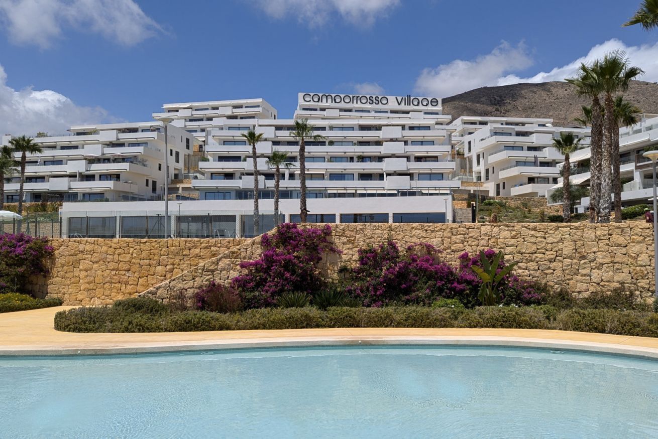 Un moderno complejo hotelero llamado Camorrosso Village con varios balcones, piscina y exuberante jardinería.