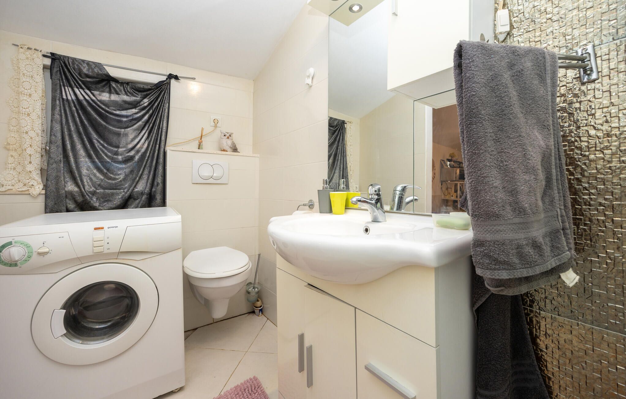 Une salle de bain moderne équipée d’un lave-linge, de toilettes, d’un lavabo et d’un porte-serviettes.