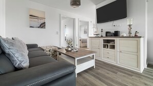 Un salon moderne avec un canapé gris, une table basse en bois et un téléviseur fixé au mur.