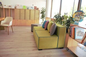 A cozy room with a yellow sofa, a wooden cabinet with drawers, a bookshelf, and a window with natural light.