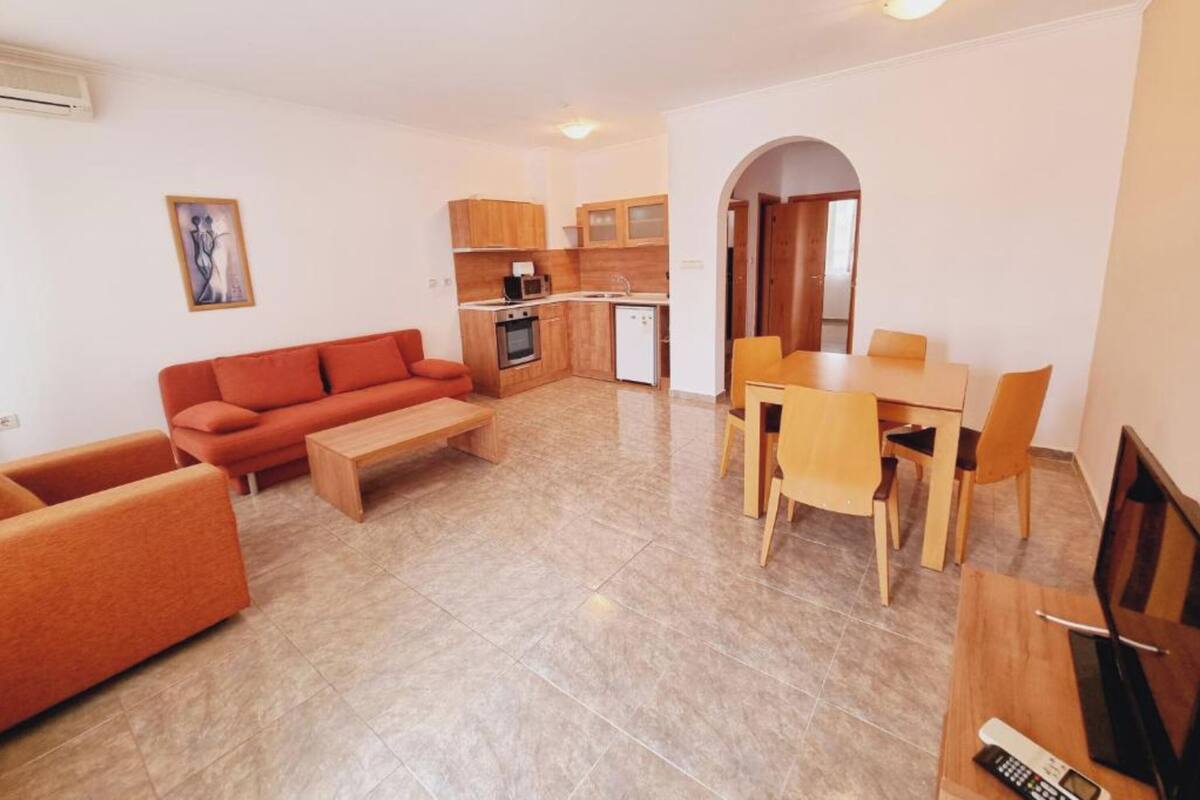 A compact living space with a sofa, a dining table with chairs, a kitchenette, and a small TV.