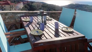 A wooden table with plates, cups, and a candle, overlooking a coastal view with buildings in the distance. - Vacation home Danese by Interhome (Civezza)