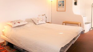 A bedroom with a large bed, a bedside table, a floor lamp, and a small wooden bench. - Vacation home Danese by Interhome (Civezza)