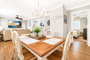 A dining area with a wooden table, white chairs, and a chandelier. - Pier Side Retreat St. Simons Island 3BR Sleeps 8 (St. Simons Island)