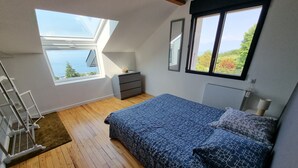 Een slaapkamer met dakraam, een bed met beddengoed met patroon, een kleine dressoir en een nachtkastje met lamp.