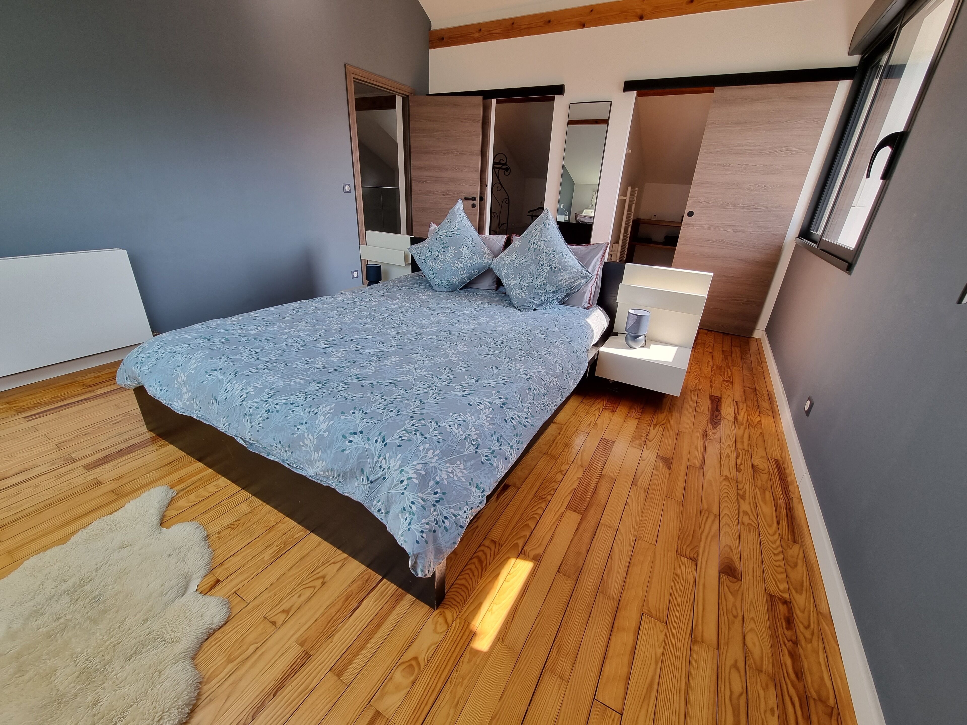 Une chambre moderne avec un grand lit, des tables de chevet, un miroir et un plancher en bois.