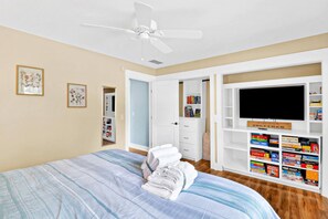 A bedroom with a bed, a ceiling fan, a TV, and a bookshelf. - Pet-Friendly Palmetto Dunes House Walk to Beach & (Hilton Head Island)