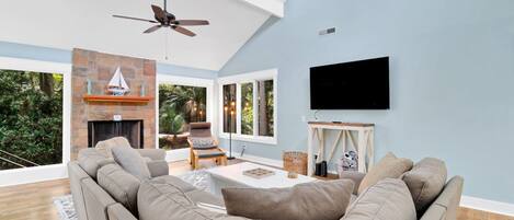 Una sala de estar con techo alto, chimenea, sofá, televisor y vistas al exterior.