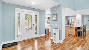 A spacious living area with hardwood flooring, a white door with stained glass, and a kitchen with white cabinets and a wooden dining table. - Pet-Friendly Palmetto Dunes House Walk to Beach & Golf (Hilton Head Island)
