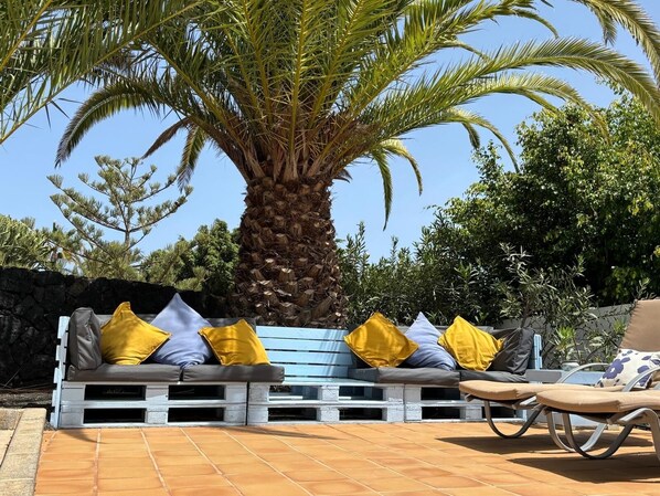 A patio area with a wooden bench and lounge chair, a palm tree, and a stone wall. - Relaxing Villa Vista a la Montana, Heated Private Pool short walk from seafront (Playa Blanca)