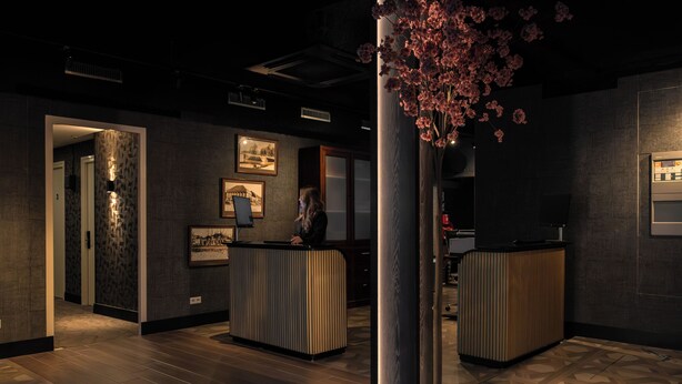 A reception area with a reception desk, framed pictures on the wall, and a decorative floral arrangement. - Hotel Twenty-Three Amsterdam Airport (Hoofddorp)