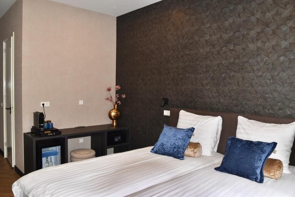 Une chambre d’hôtel avec un lit, une table de chevet ornée d’un vase et un mur au motif texturé.