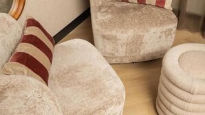 A room with a beige armchair and ottoman, a striped pillow, and a mirror reflecting the room. - Hotel Twenty-Three Amsterdam Airport (Hoofddorp)