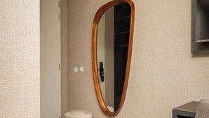A modern hotel room with a wooden-framed mirror, a small round ottoman, and a dark-colored desk. - Hotel Twenty-Three Amsterdam Airport (Hoofddorp)