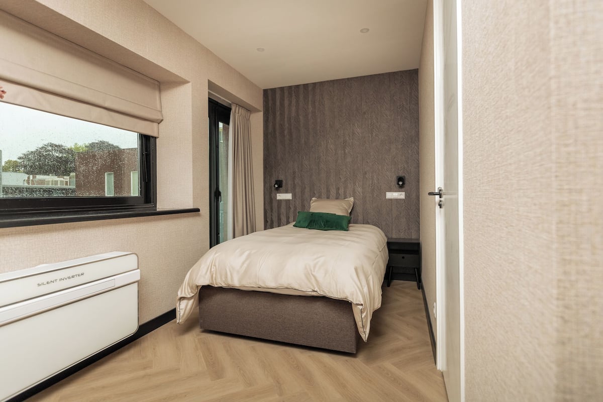 A bedroom with a bed, a window with a blind, a bedside table, and a wardrobe.