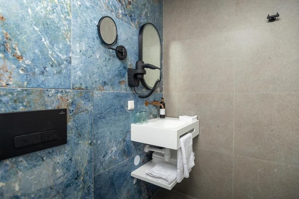 A bathroom with a marble wall, a white sink, two mirrors, and a towel rack.