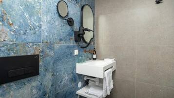 A bathroom with a marble wall, a white sink, two mirrors, and a towel rack.