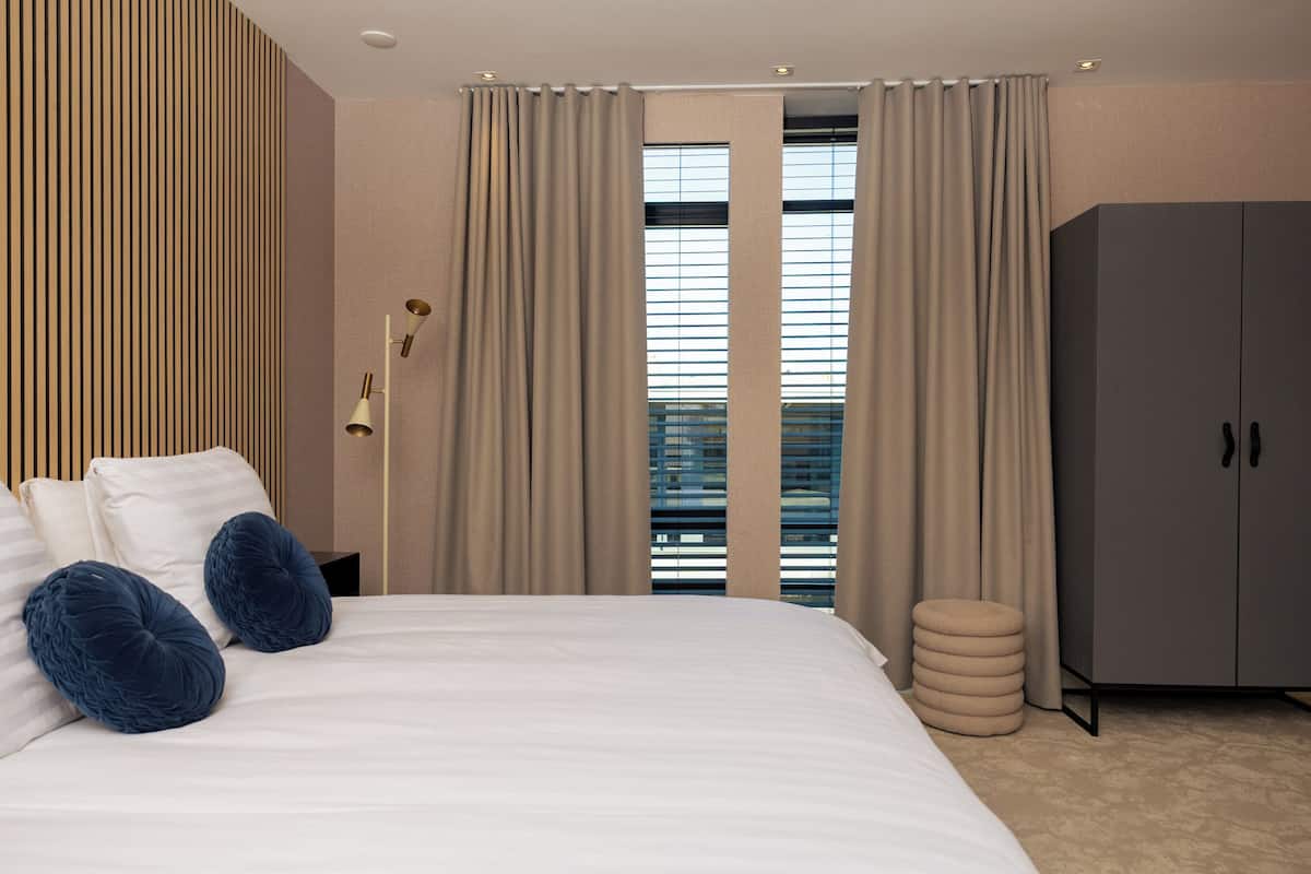 A modern hotel room with a large bed, a wardrobe, and a window with curtains.