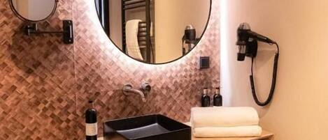 Une salle de bain moderne avec un meuble-lavabo en bois, un miroir rond et un sèche-cheveux fixé au mur.