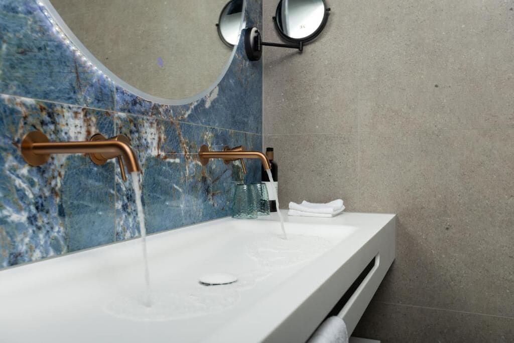 Un baño con lavamanos blanco, detalles en cobre y un respuesto de mármol azul.