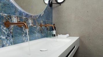 Un baño con lavamanos blanco, detalles en cobre y un respuesto de mármol azul.