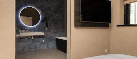 A bedroom with a bed, a TV mounted on the wall, and a bathroom visible through an open door.