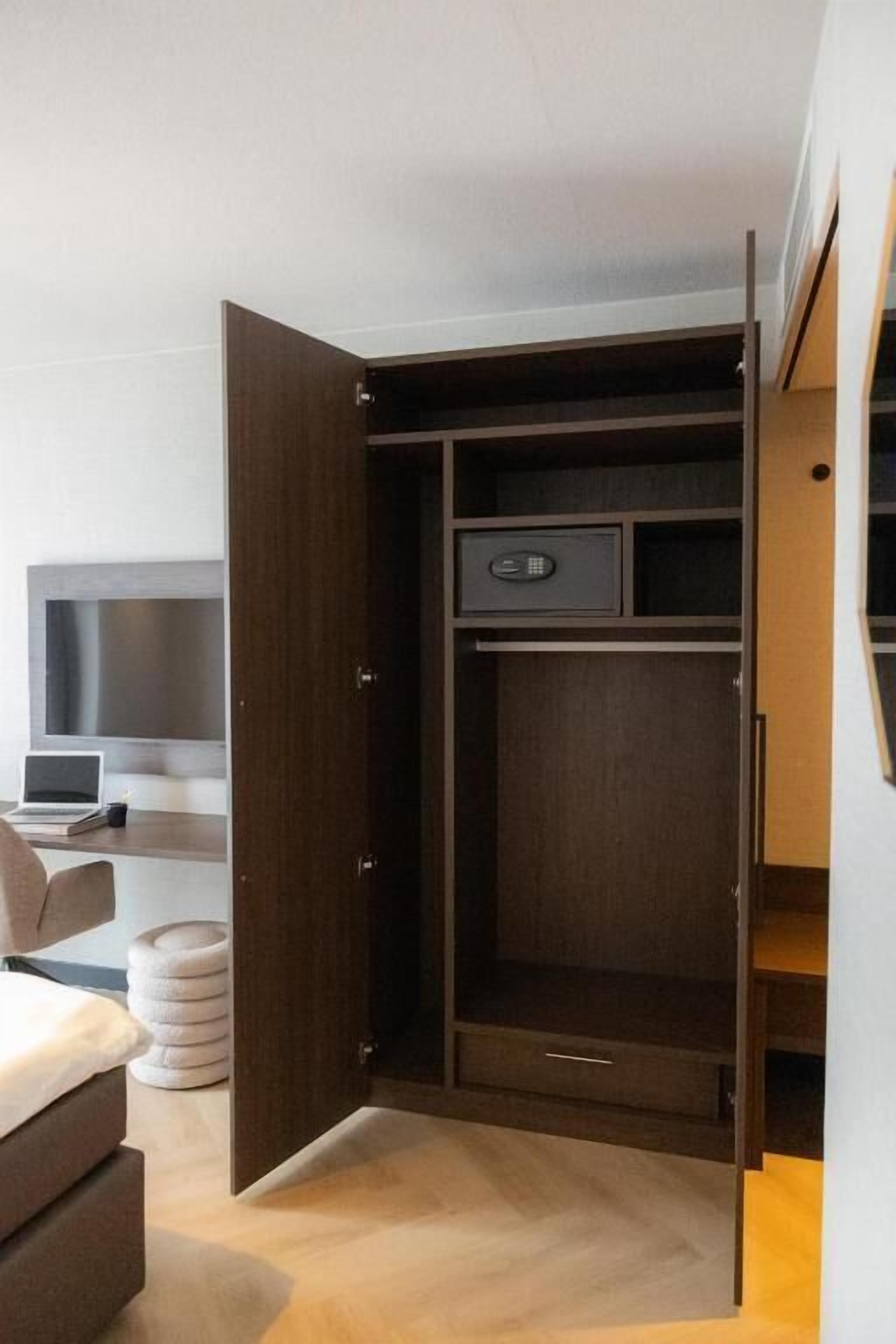 A modern bedroom with a built-in wardrobe, a bedside table, a chair, and a TV.