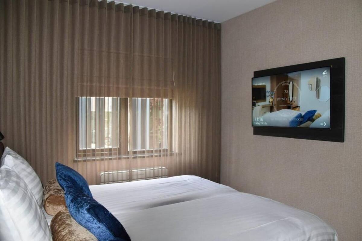 A hotel room with a large bed, a television mounted on the wall, and a window with blinds.