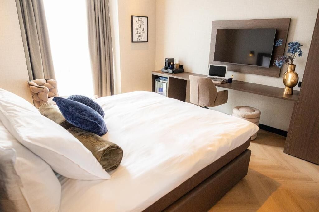 A hotel room with a bed, a desk with a computer, a TV, and a vase with flowers.