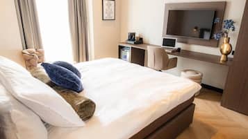 A hotel room with a bed, a desk with a computer, a TV, and a vase with flowers.