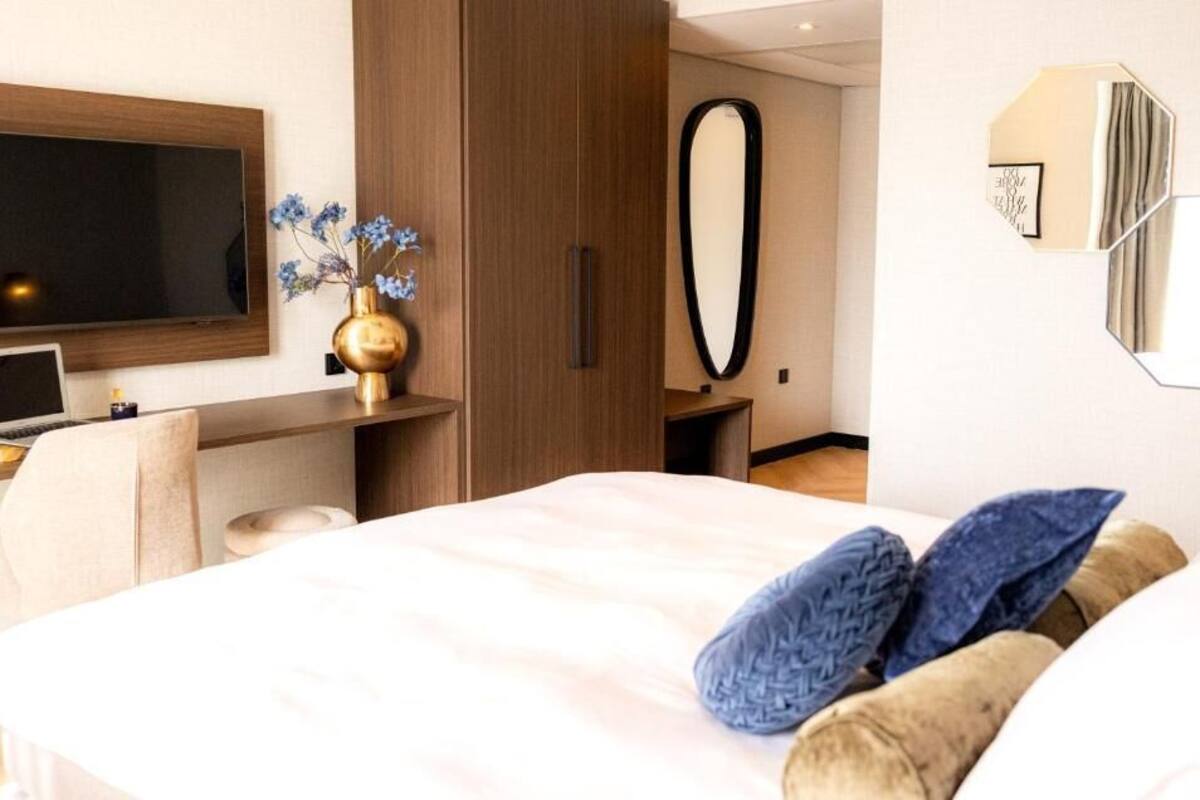 A modern hotel room with a bed, a desk, a TV, and a mirror.
