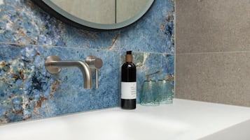 Un baño con lavamanos blanco, salpicadero de mármol azul, espejo redondo y una botella de jabón de manos.