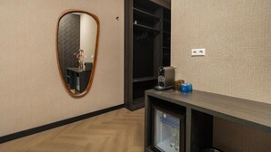 A hotel room with a wooden floor, a mirror, a wardrobe, and a small shelf with a coffee maker and bottles. - Hotel Twenty-Three Amsterdam Airport (Hoofddorp)