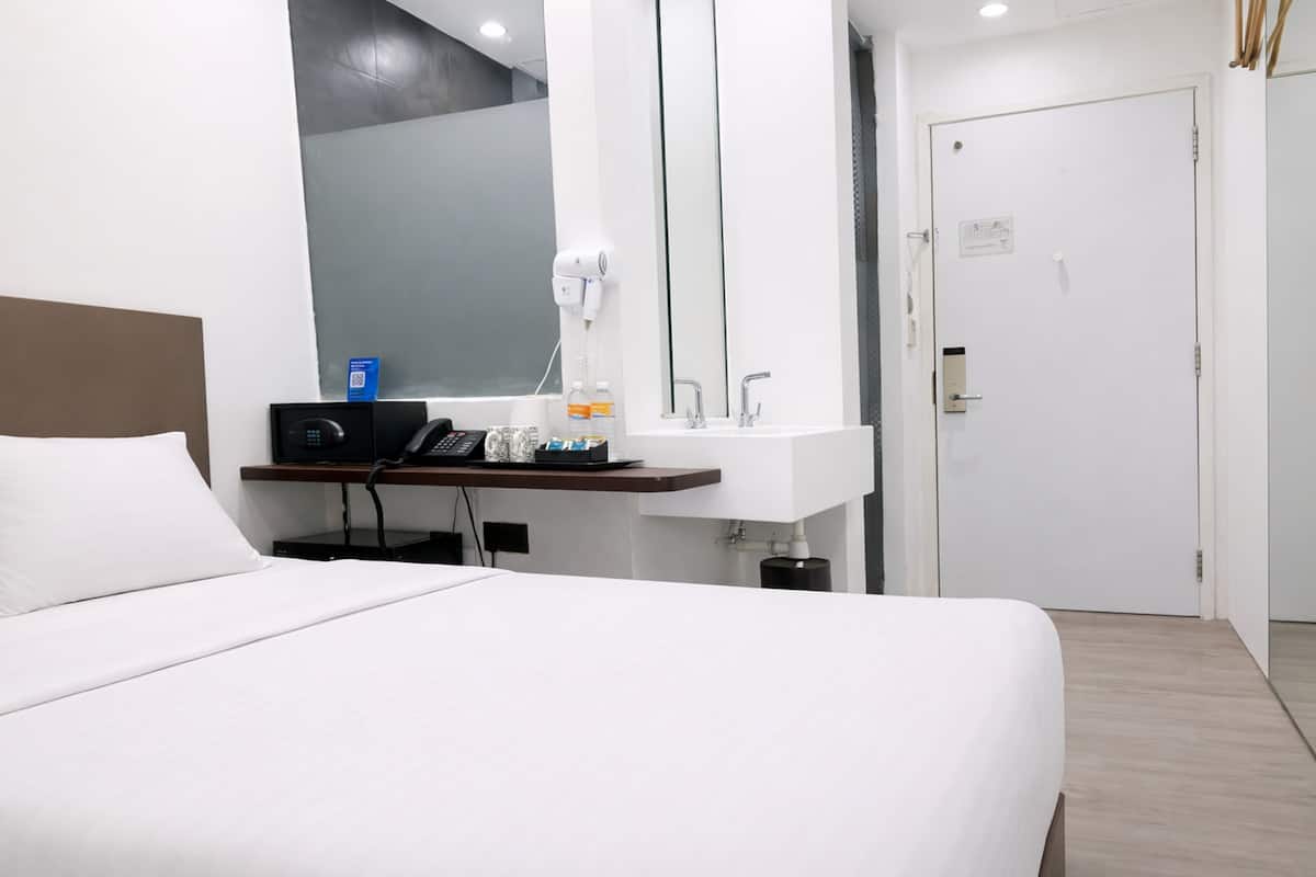 A hotel room with a bed, a desk with a phone, a mirror, a sink, and a door.