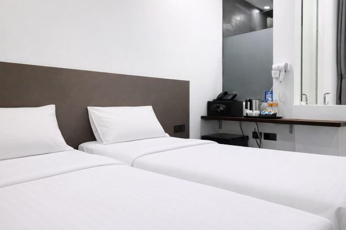 Habitación de hotel con dos camas individuales, un escritorio pequeño con un teléfono y artículos de aseo, y un espejo sobre el escritorio.