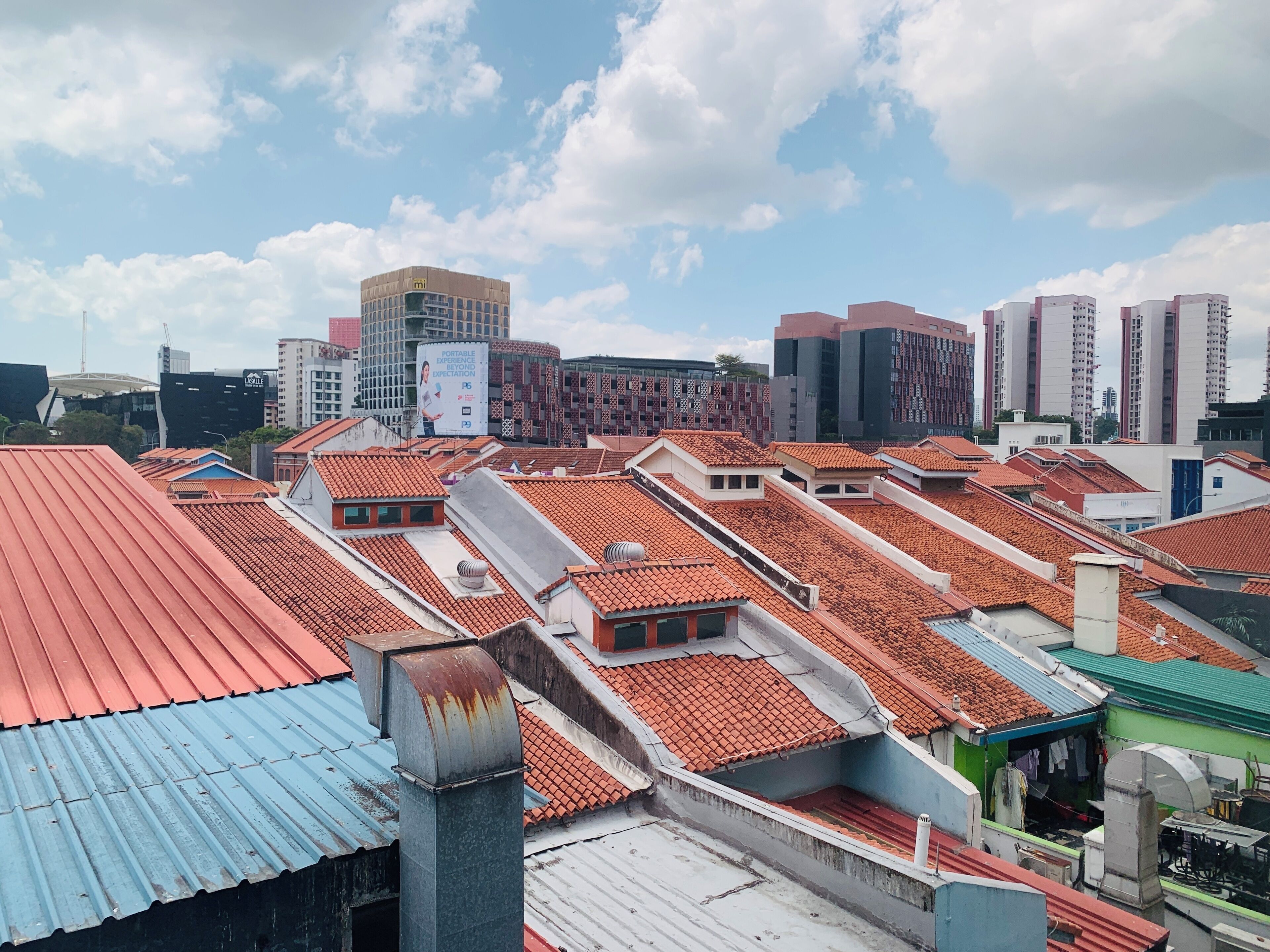 A cityscape with red-tiled rooftops and modern high-rise buildings in the background.