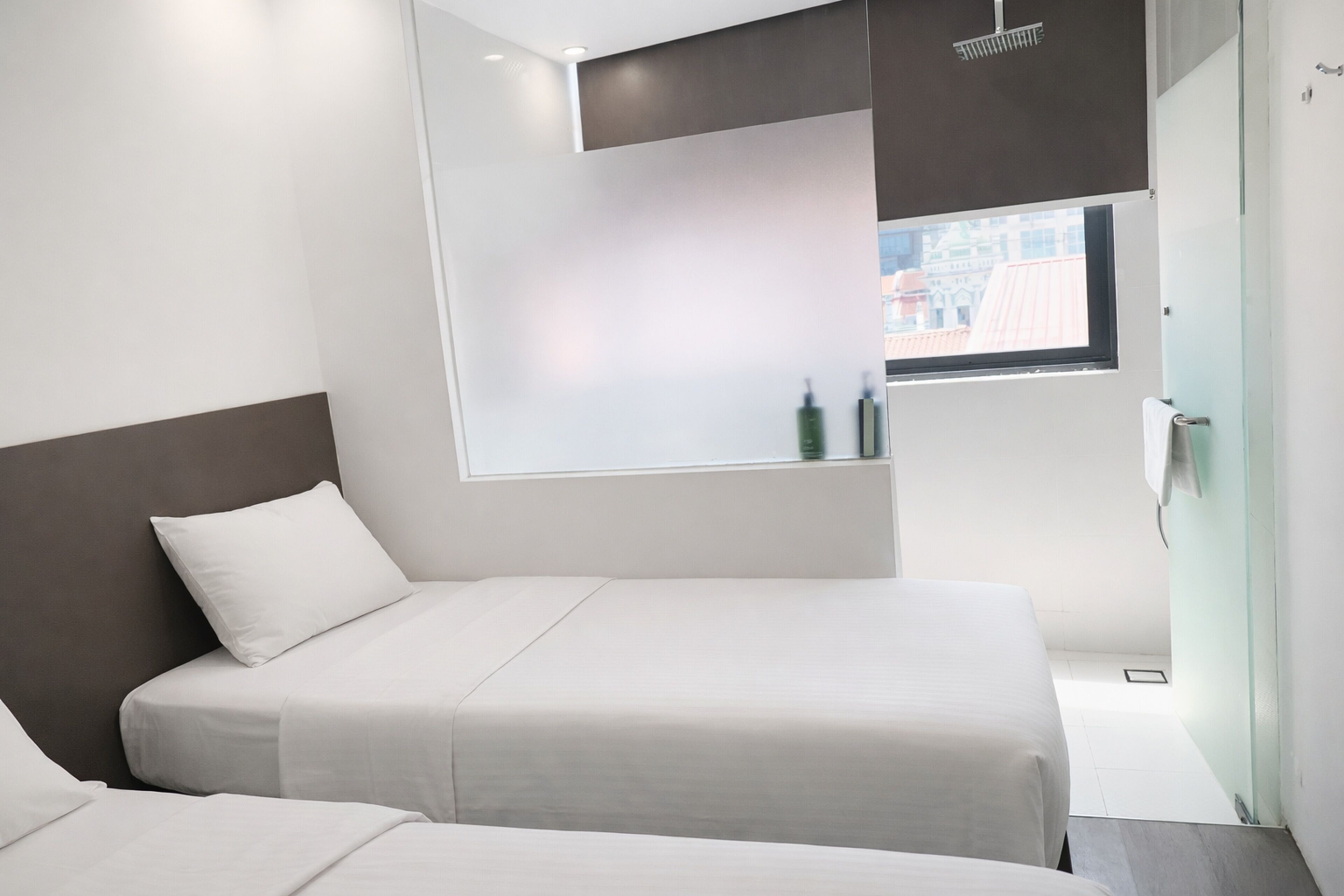 A modern hotel room with two beds, a large window, and a view of the city.