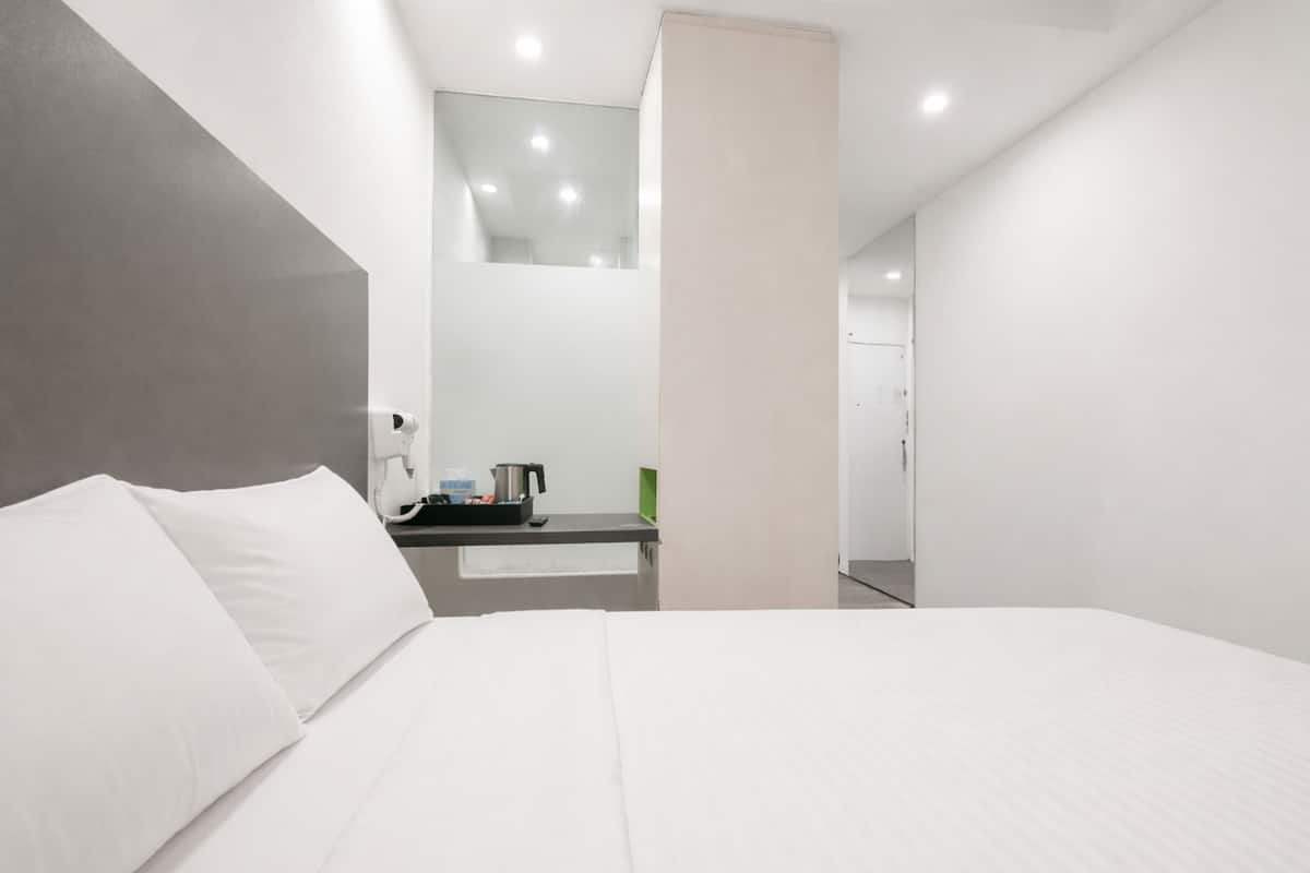 A modern hotel room with a large bed, a small bedside table with a kettle, and a mirror above the bed.