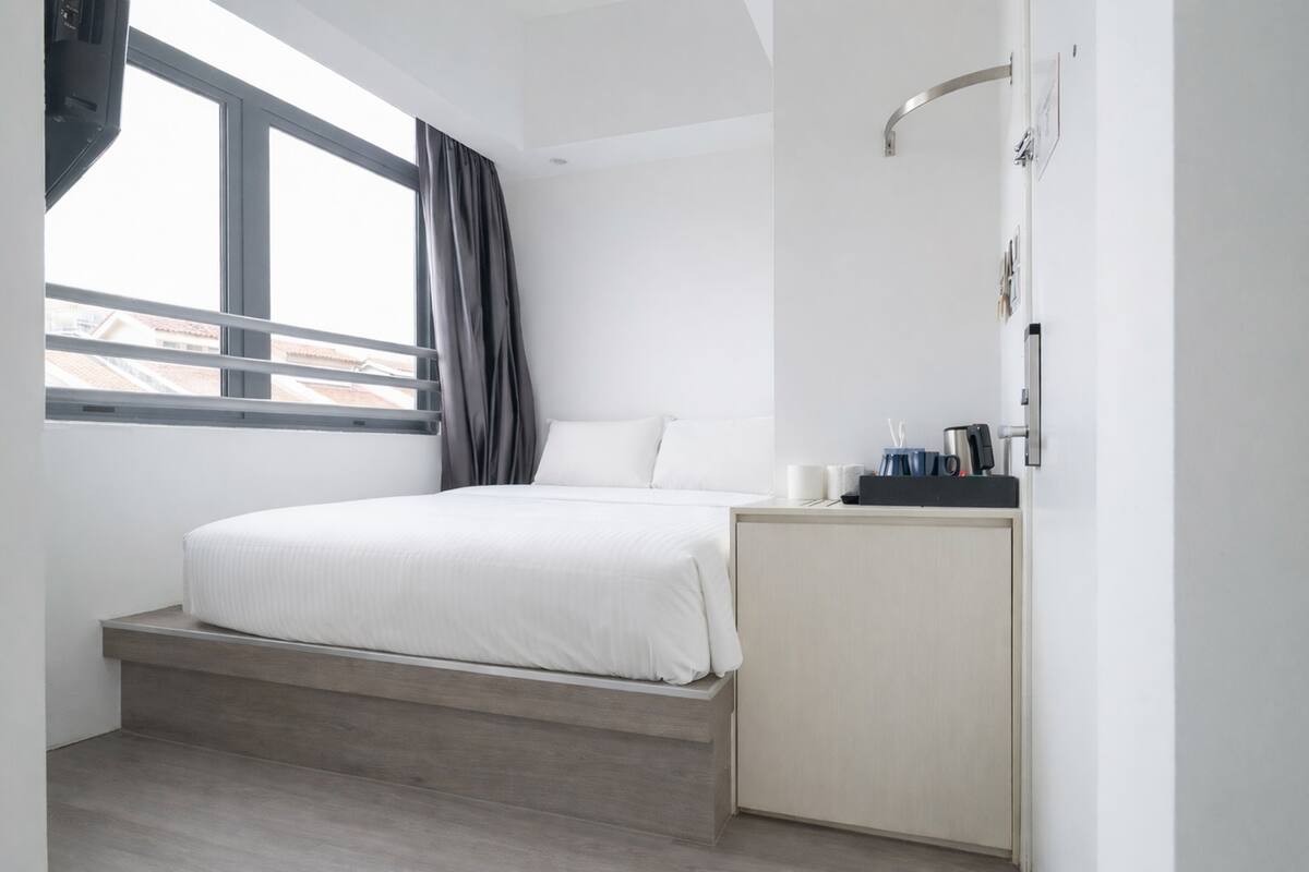 A modern hotel room with a bed, a small desk, and a window with curtains.