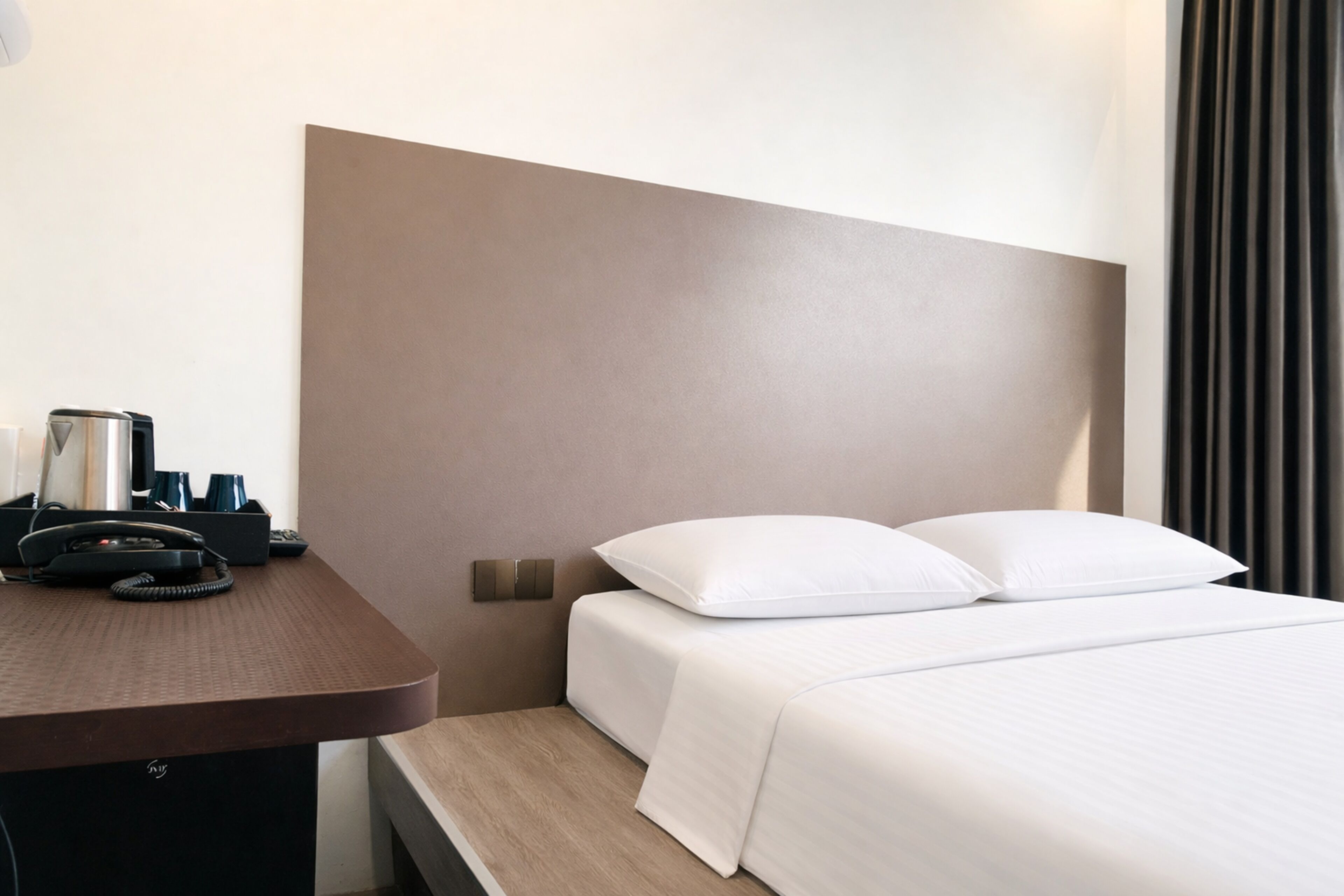 A hotel room with a bed, a desk with a telephone and a coffee maker, and a headboard.