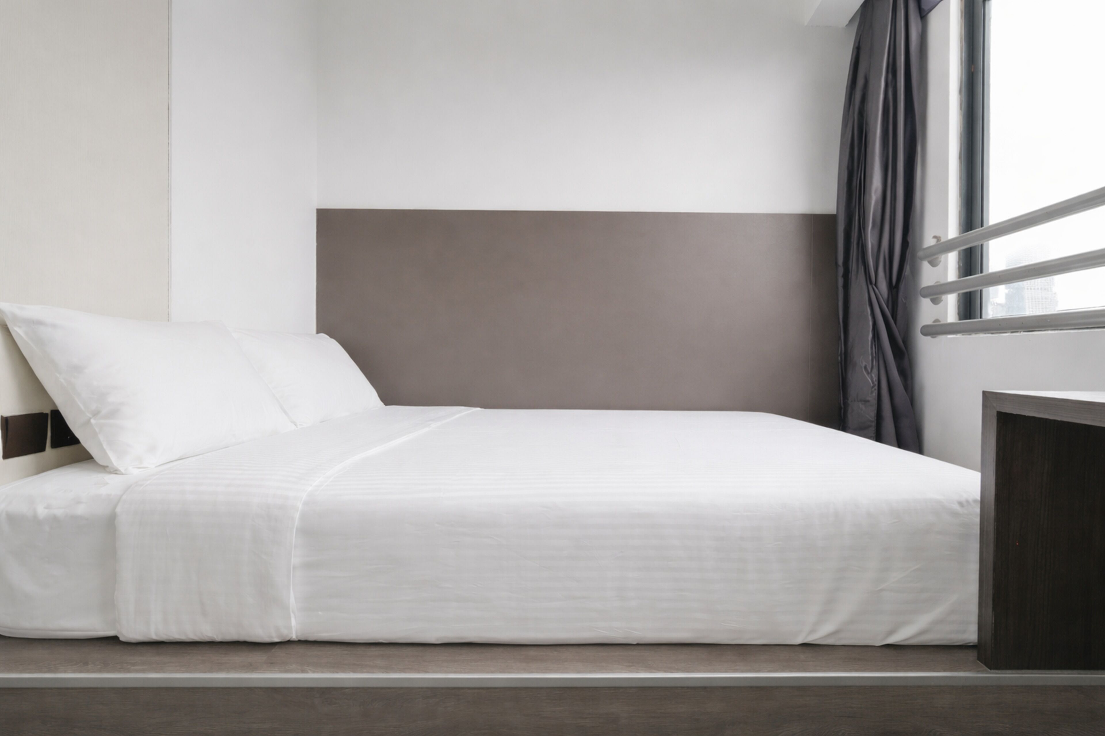 A neatly made bed with white bedding and a dark headboard in a hotel room.