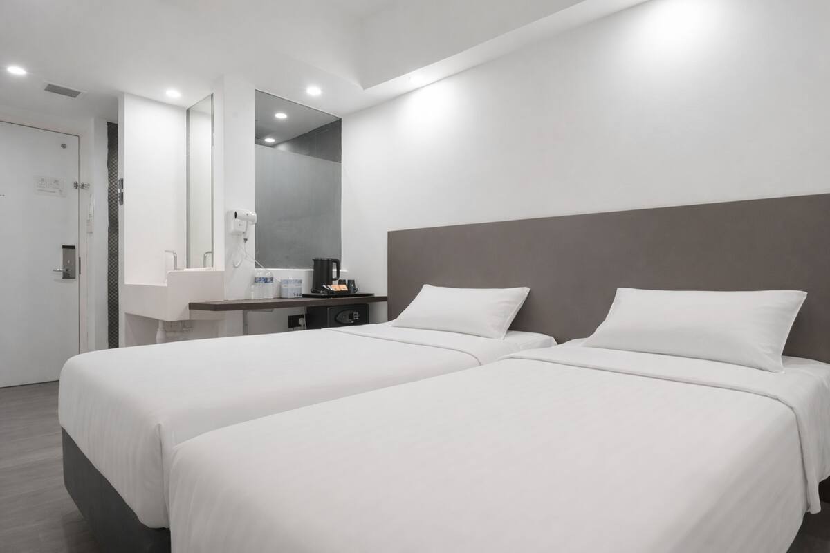 A modern hotel room with two beds, a large mirror, a small desk with a coffee maker, and a shower area.