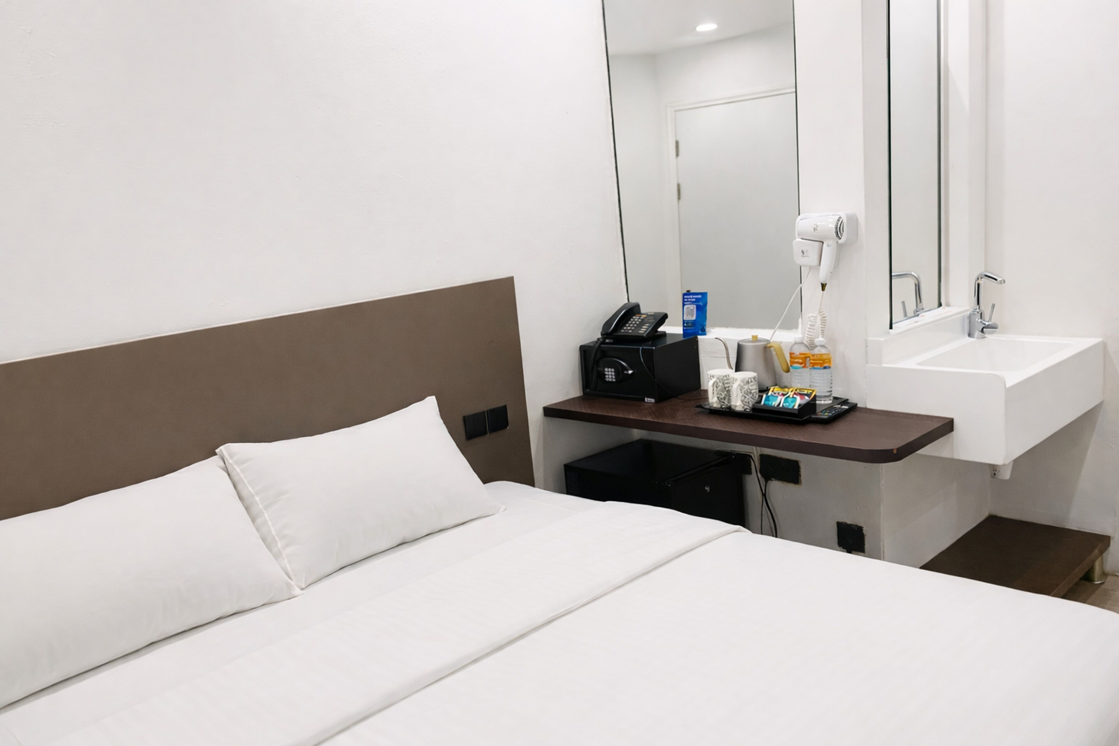 Habitació d'hotel amb un llit, una taula de nit amb un telèfon, un assecador i un mirall.