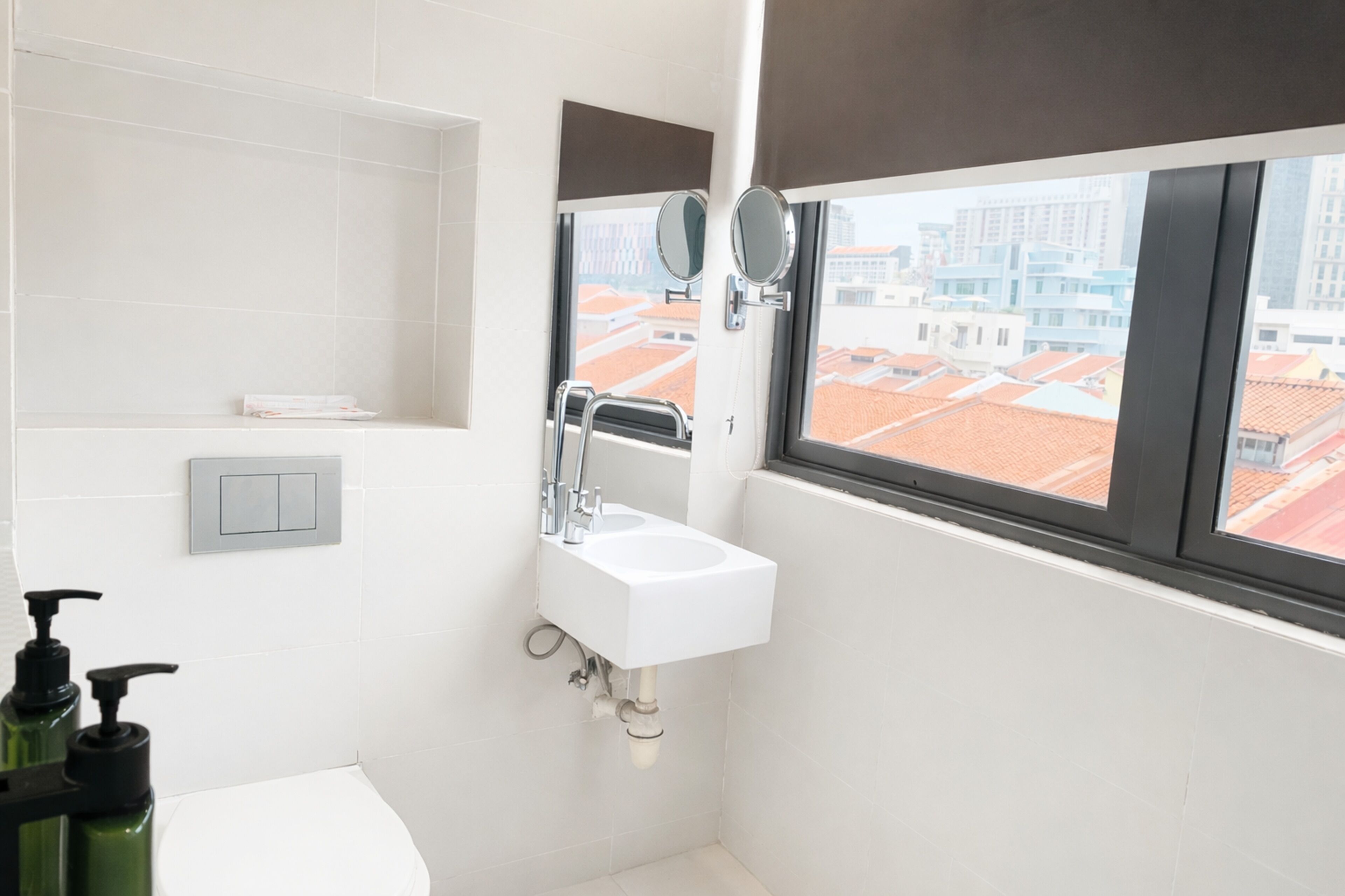 A modern bathroom with a white sink, two mirrors, and a window with a city view.