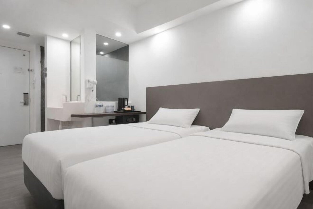 A modern hotel room with two beds, a large mirror, a small desk, and a bathroom.